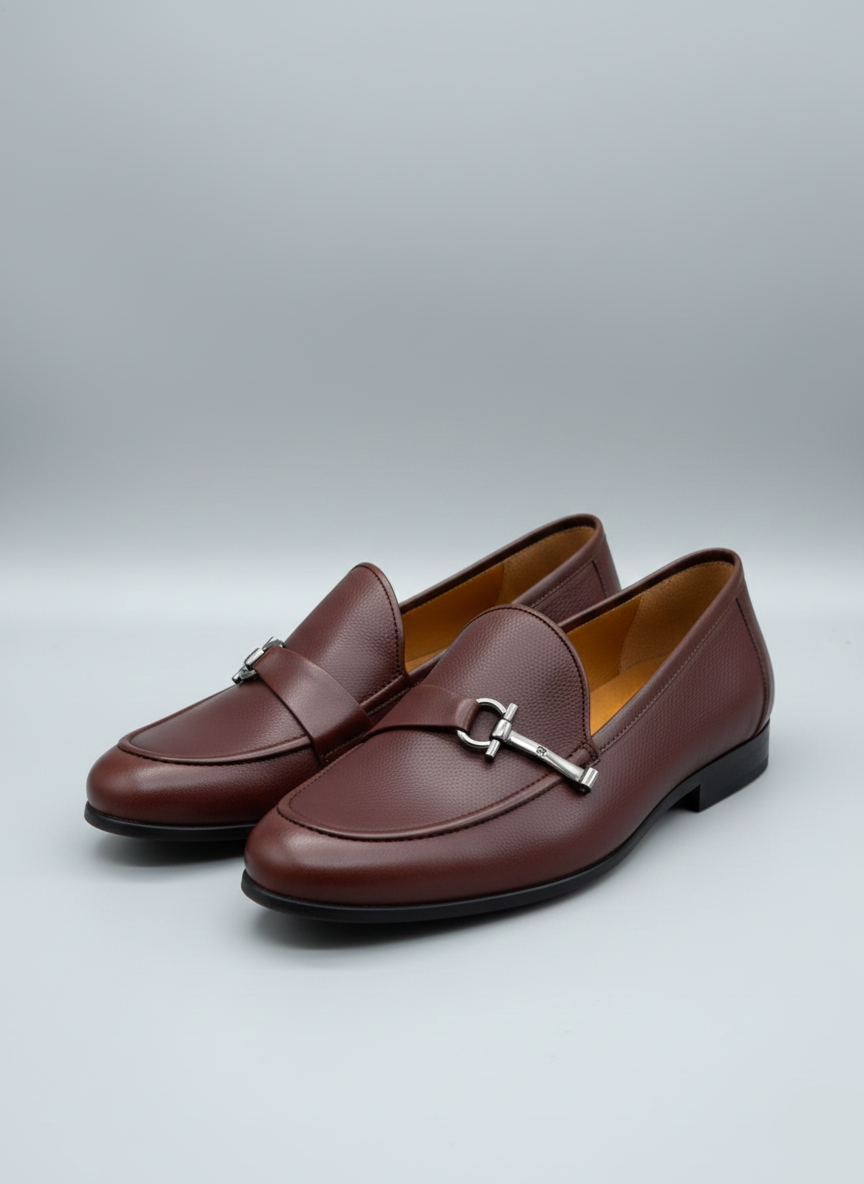 Pair of brown leather loafers with a silver buckle on a light gray background